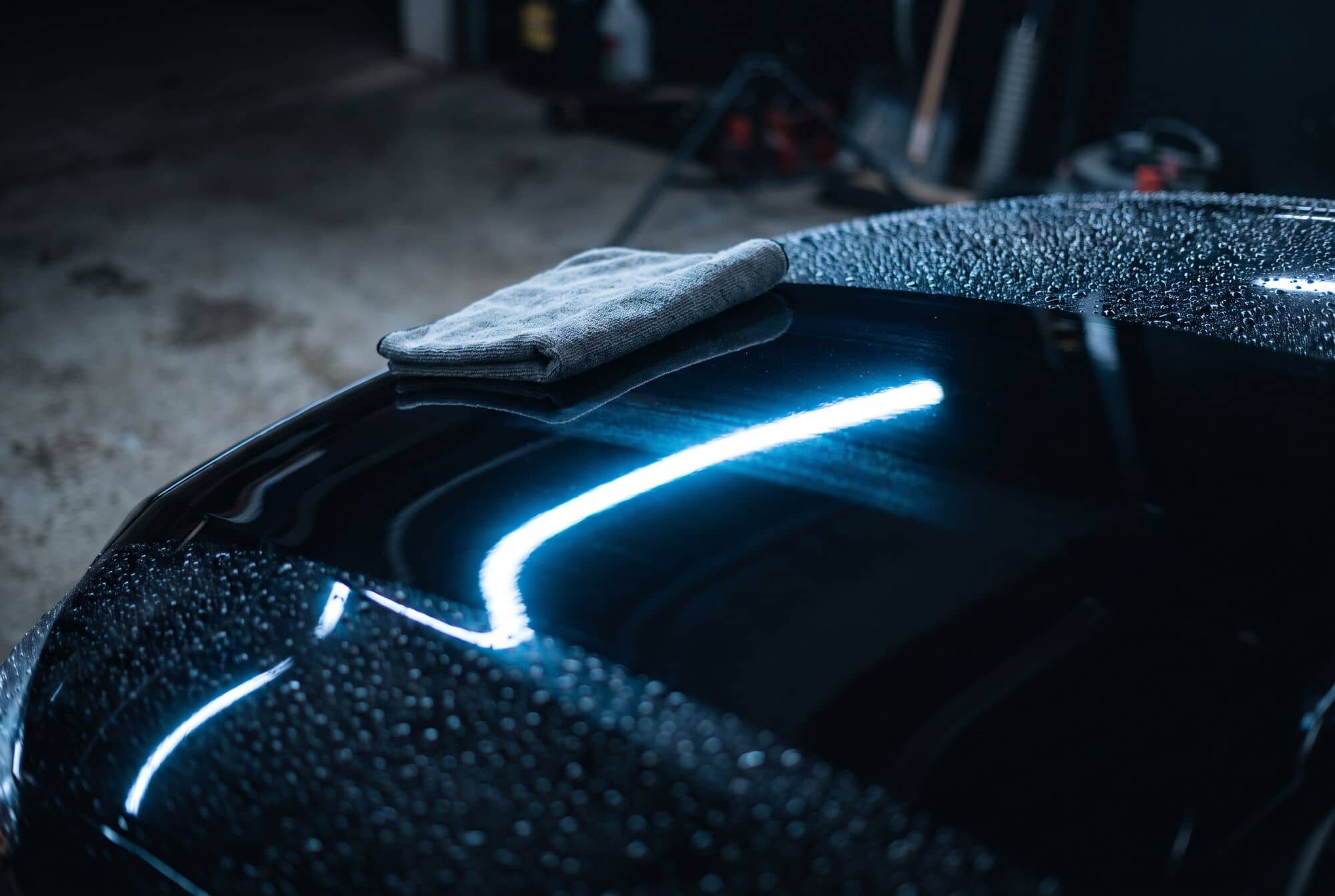 Pano de microfibra sobre o capô preto e espelhado de um carro, com reflexos de luz azul