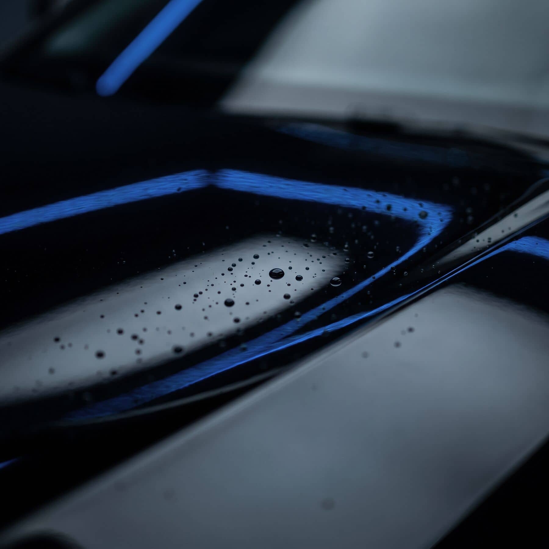 Pintura preta espelhada refletindo faixas de luz azul, com pequenas gotas de água